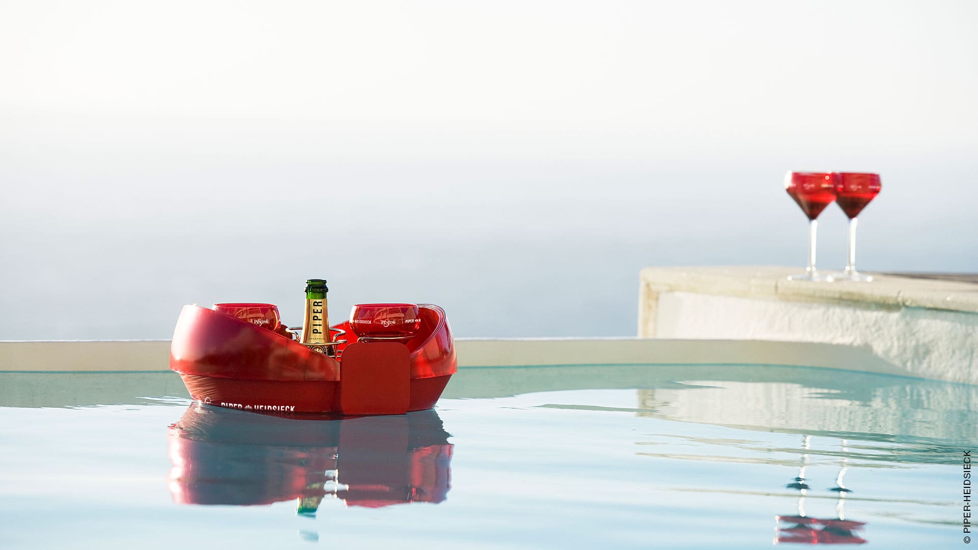 Photographie de la vasque Piper flottant dans une piscine. On peut apercevoir deux verres en haut à droite de l'image